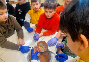 Grupa dzieci obserwująca wynik swojego doświadczenia, czyli masę przypominającą ciasto czekoladowe.