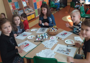 Na zdjęciu grupa dzieci znajdujących się przy okrągłym stoliku i wykonujących prace plastyczne techniką malowania na szkle.