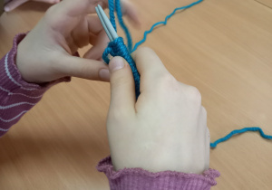 Na zdjęciu ręce dziewczynki robiącej na drutach. W oddali widać niebieski kłębek wełny.
