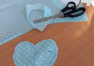 Zdjęcie wyciętego serca z tkaniny, a obok szpilki i nożyczki.